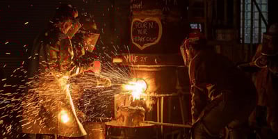Workers at a foundry handle molten metal as sparks fly, showcasing factors that impact investment casting cost.