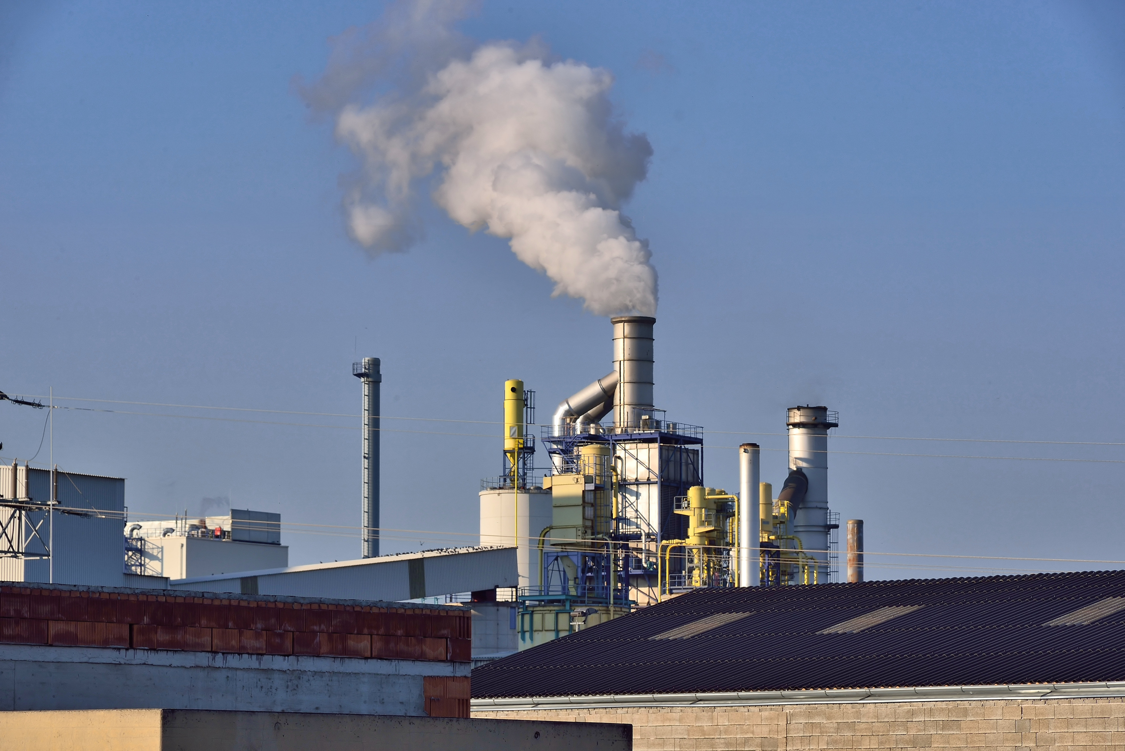 Industrial factory with smokestack releasing a large plume of white smoke into the sky.